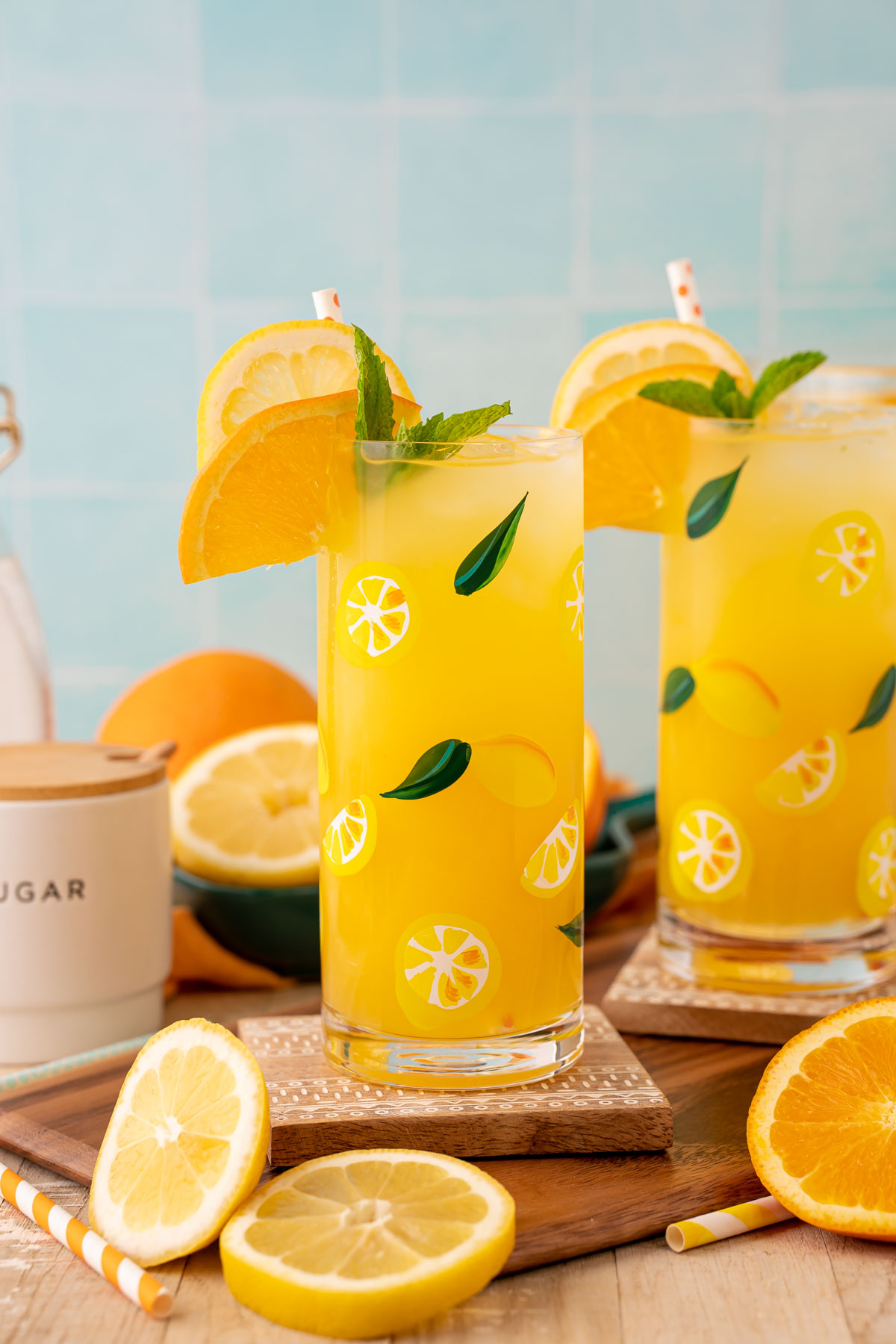 Two glasses of orangeade on coasters with citrus around them.