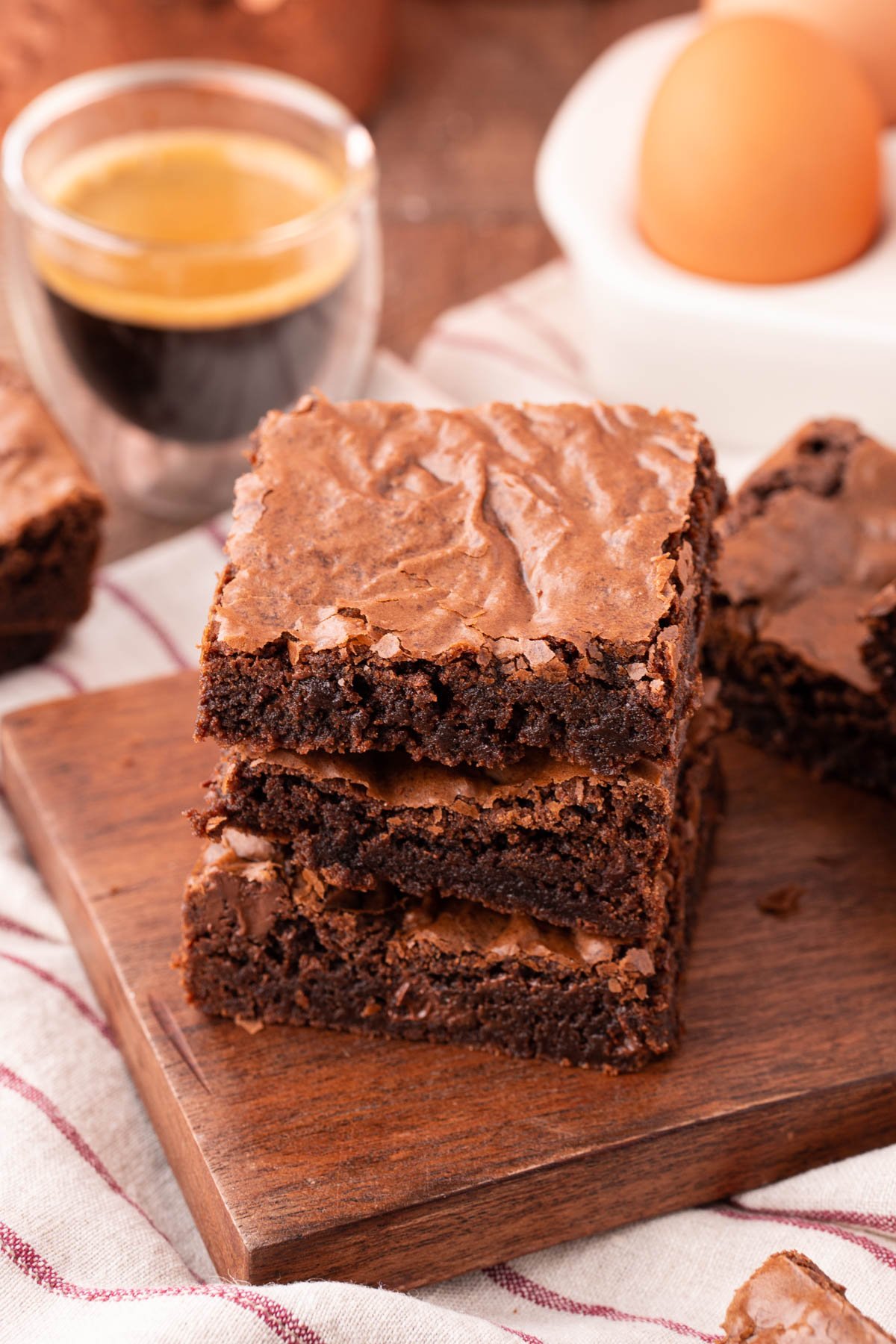 Three brownies stacked on top of each other on a wooden board.