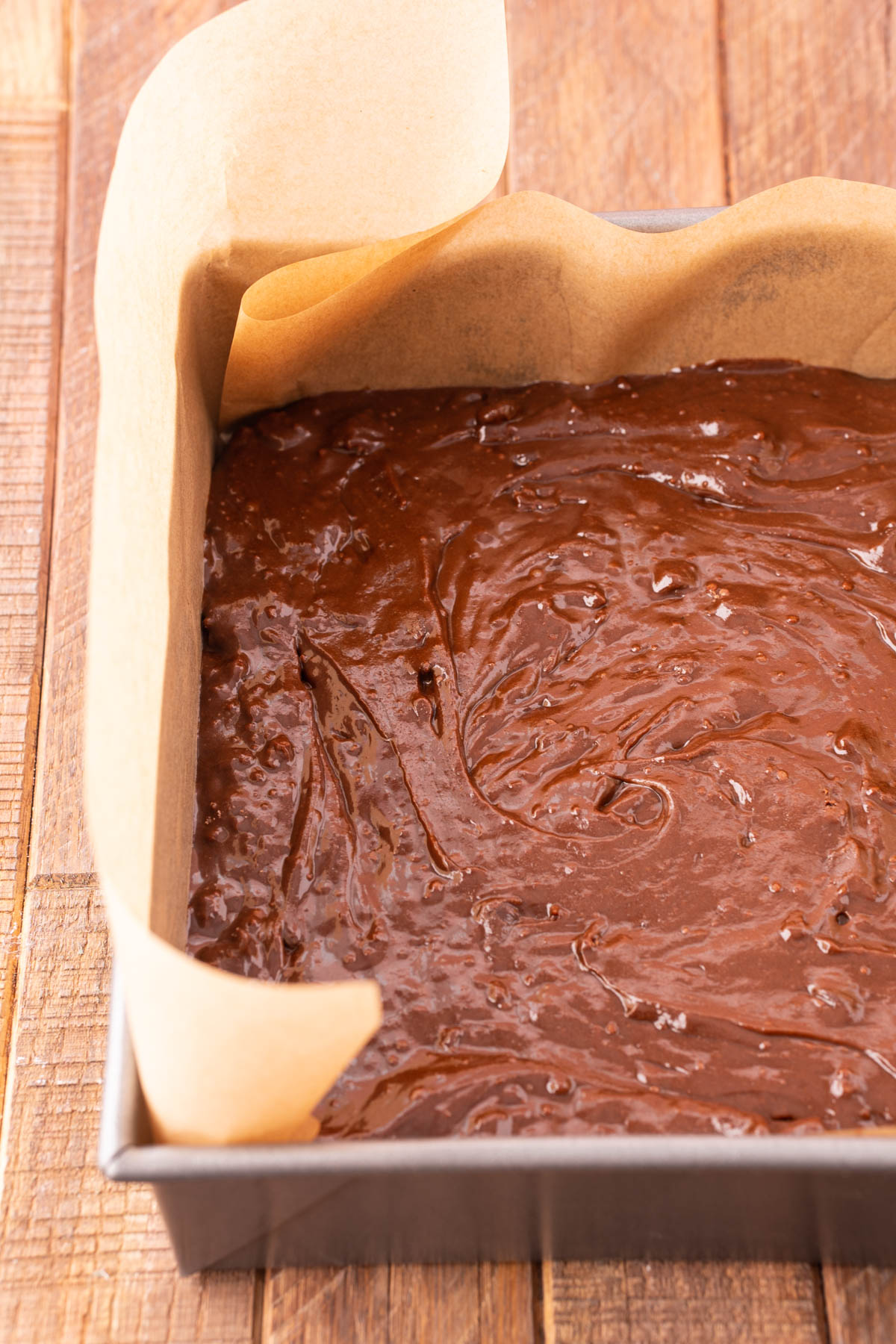 Brownie batter in a baking pan with parchment paper ready to bake.