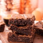 Three brownies stacked on top of each other on a wooden board.