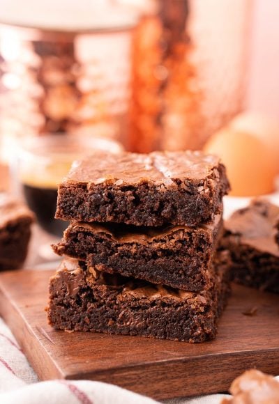 Three brownies stacked on top of each other on a wooden board.