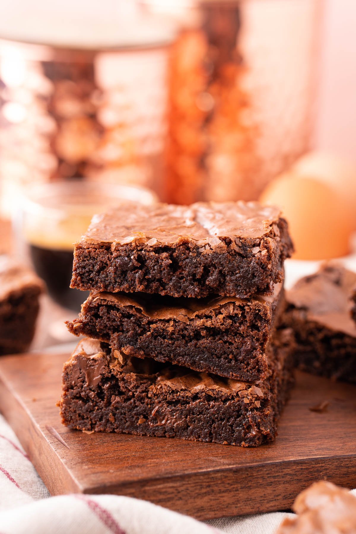 Three brownies stacked on top of each other on a wooden board.