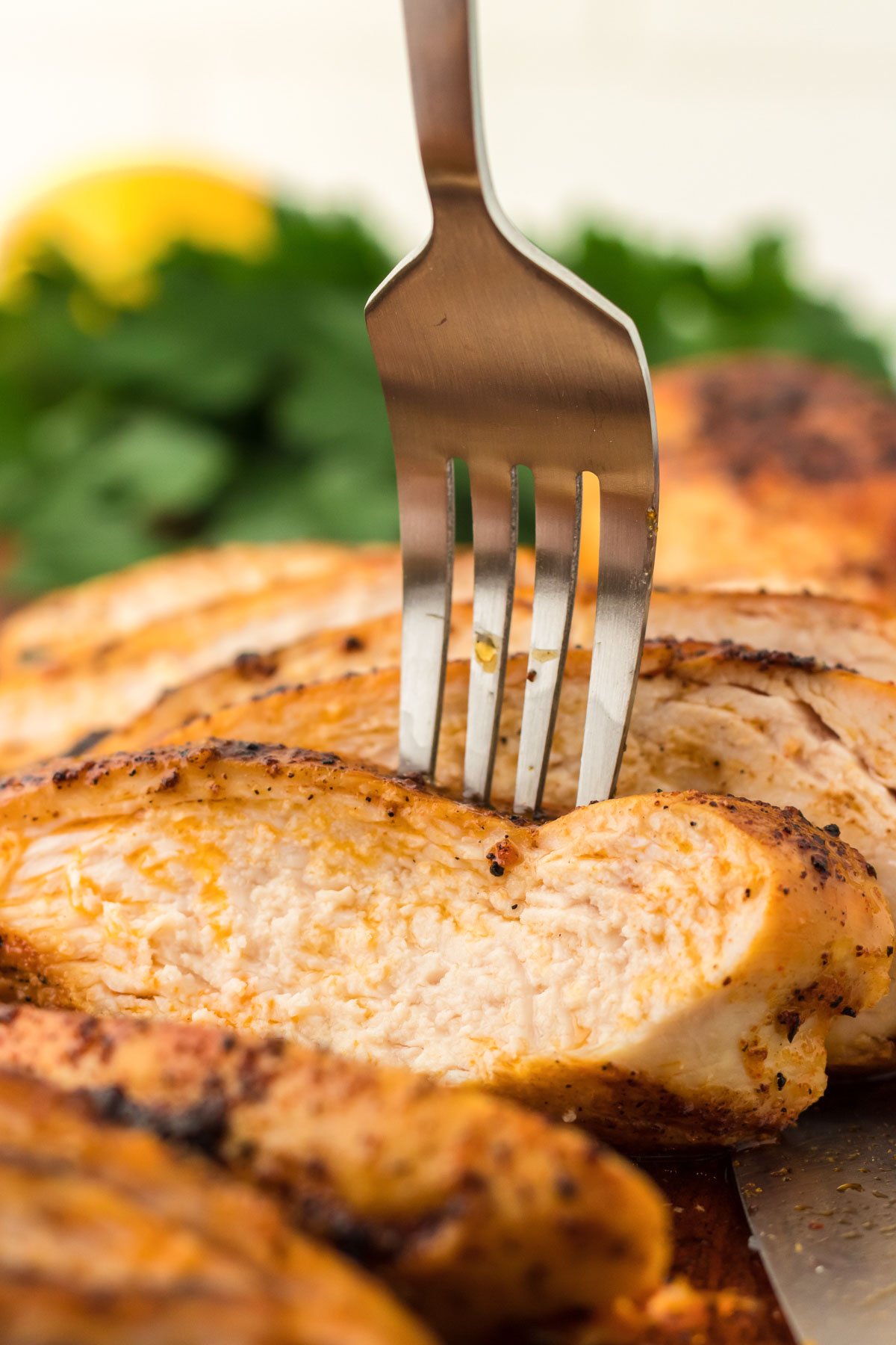 A fork sticking into a piece of sliced chicken breast.