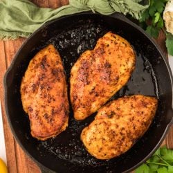 Overhead photo of three juicy chicken 101 chicken breasts in a cast iron skillet.