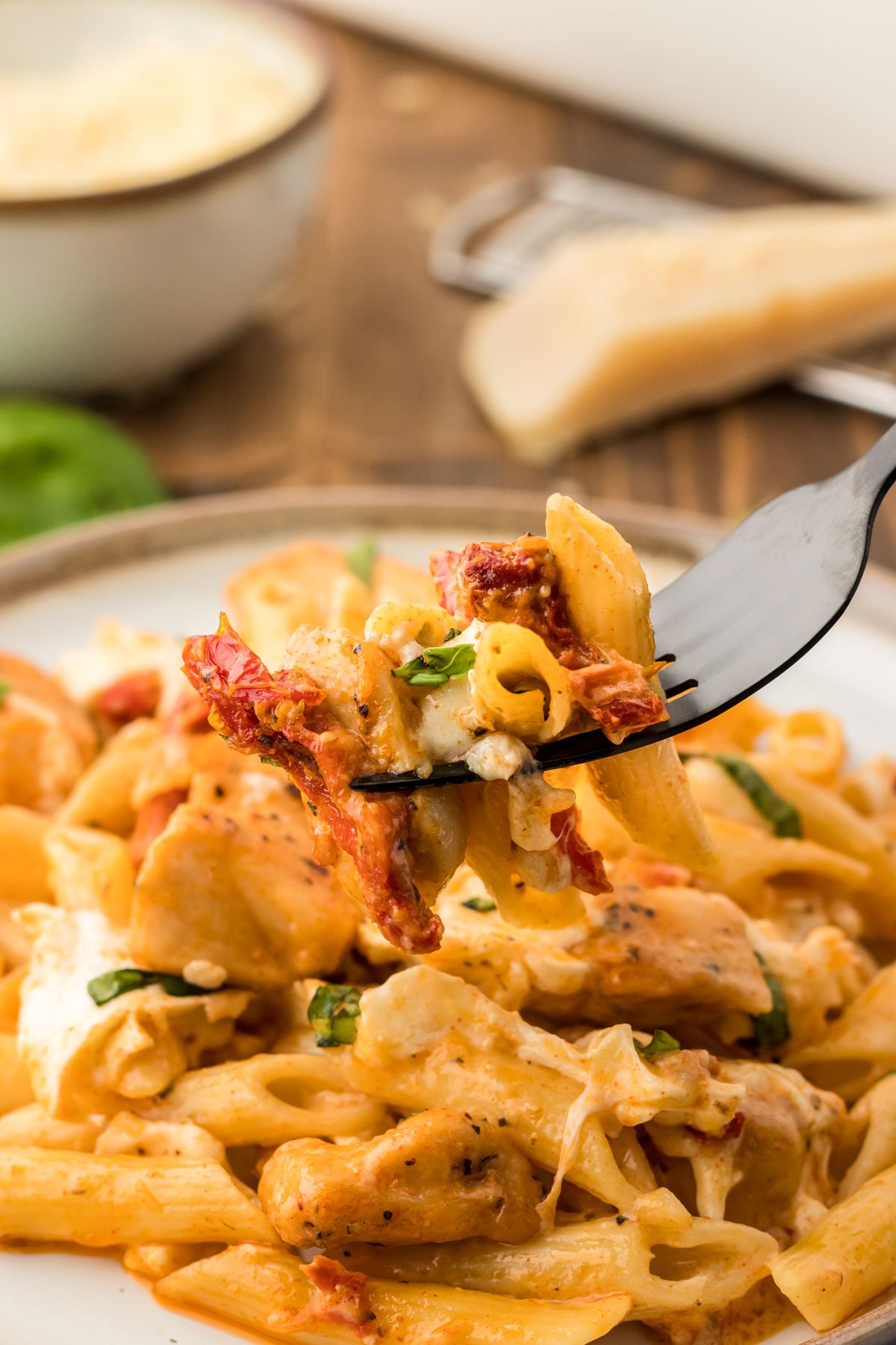 A fork taking a bite of marry me chicken pasta from a plate.