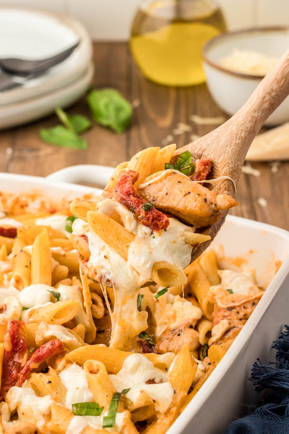 A wooden spoon scooping marry me chicken pasta out of a casserole dish.