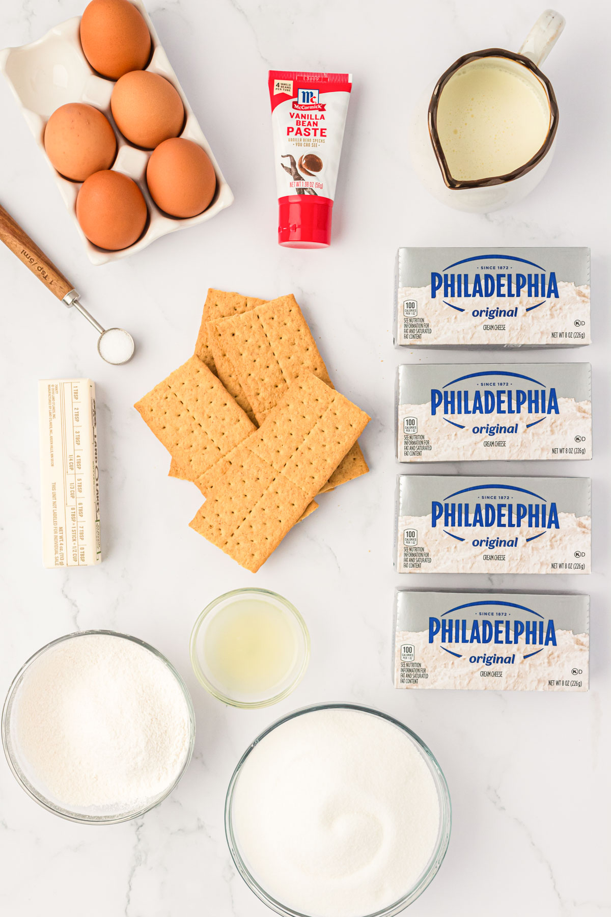 Overhead photo of ingredients to make cheesecake on a marble counter.