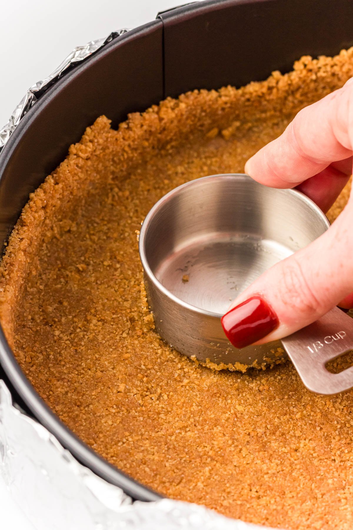 Graham cracker crust being pressed down into the bottom of a springform pan.