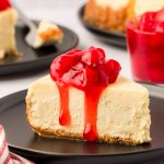 A slice of cheesecake with cherry topping on a black plate with a fork.