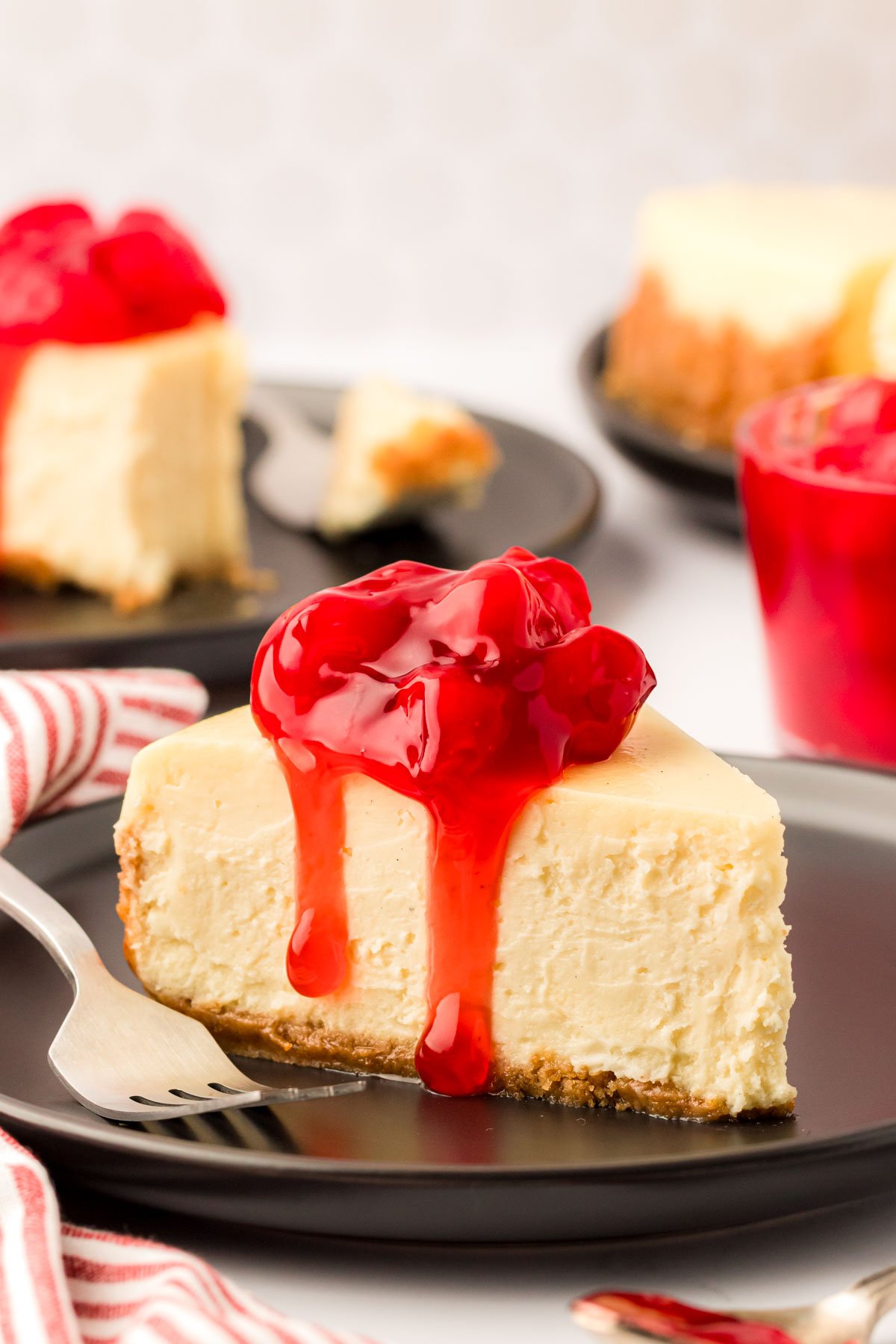 A slice of cheesecake with cherry topping on a black plate with a fork.