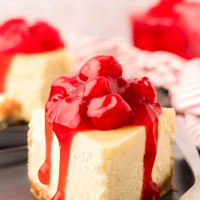A slice of cheesecake with cherry topping on a black plate with a fork.