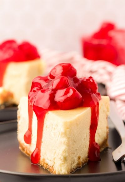 A slice of cheesecake with cherry topping on a black plate with a fork.