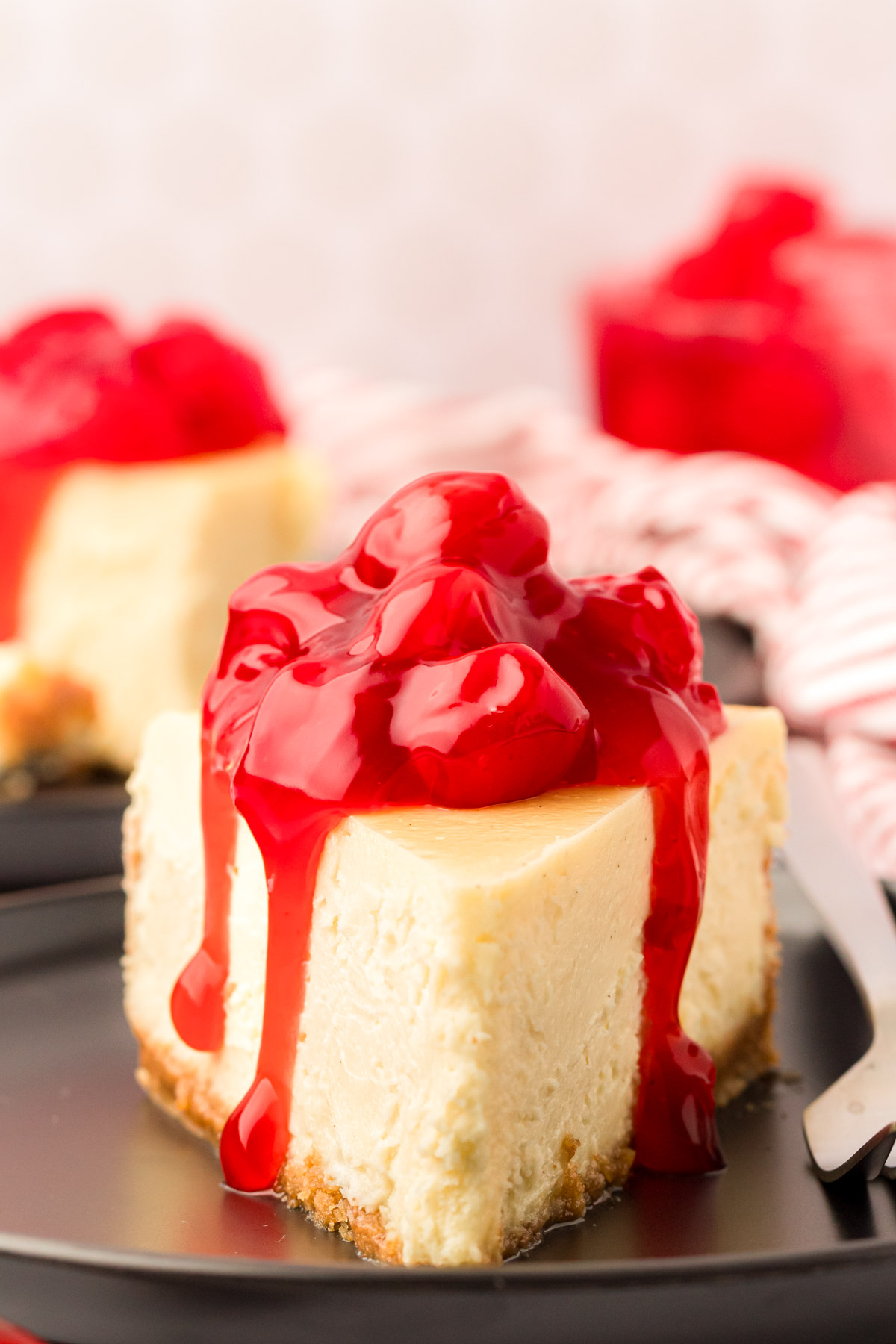 A slice of cheesecake with cherry topping on a black plate with a fork.