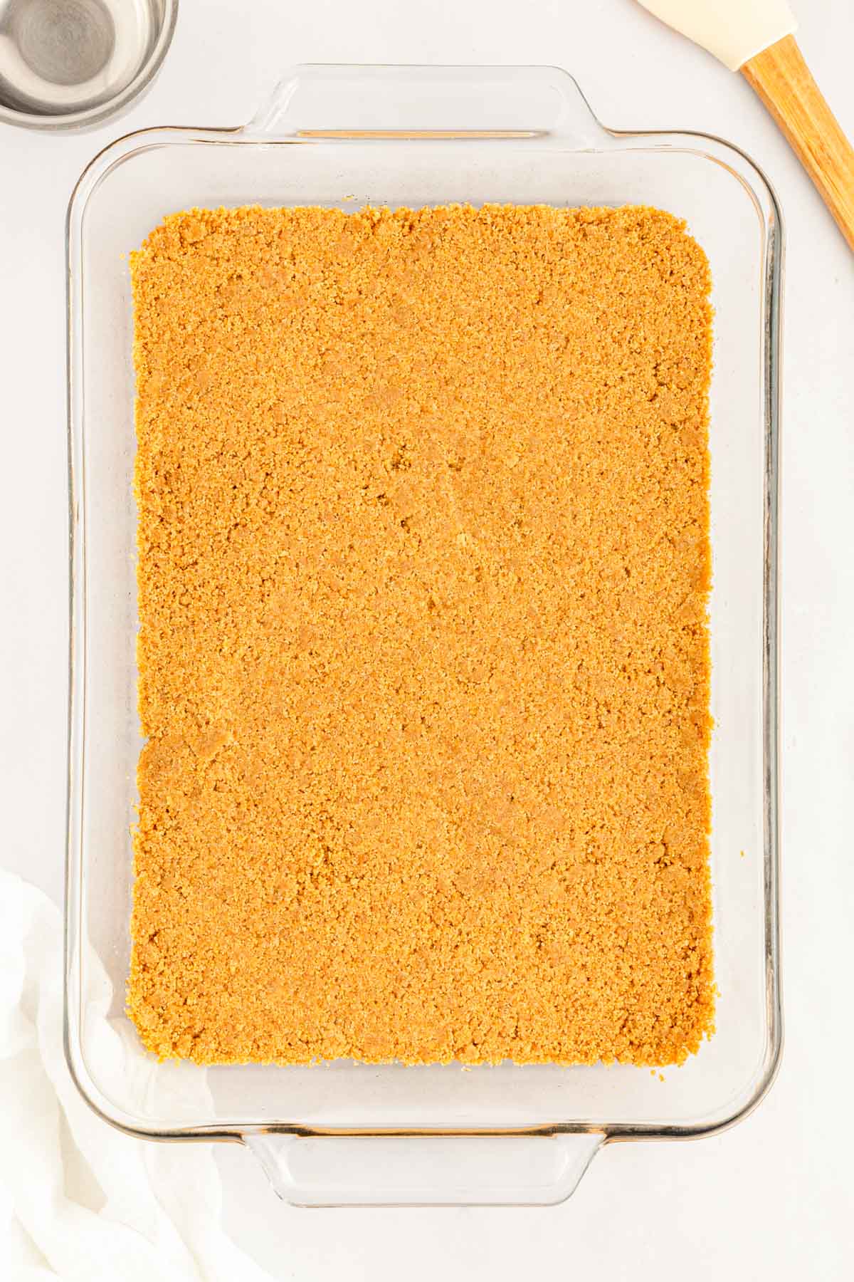 A layer of graham cracker crumbs in a glass pan.