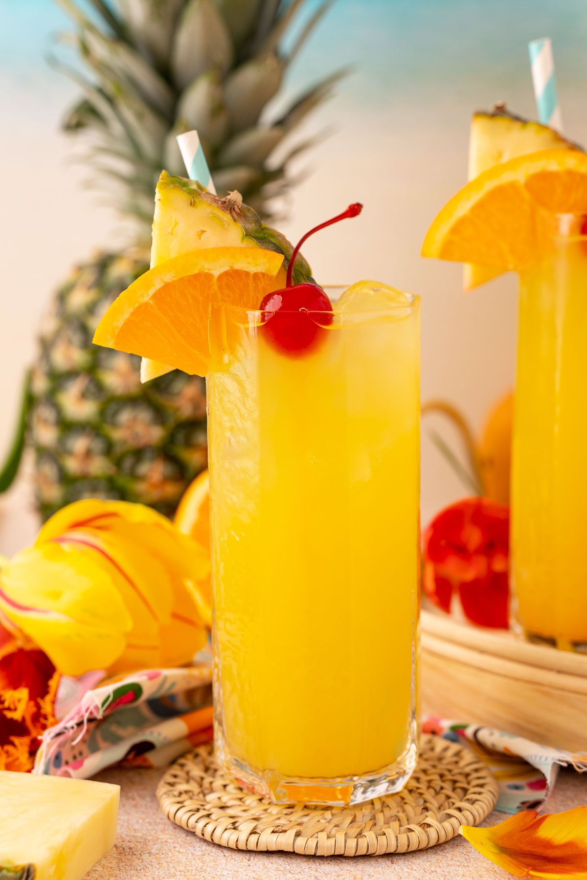 A tall glass of pineapple punch garnished with a cherry, orange slice, and pineapple wedge.