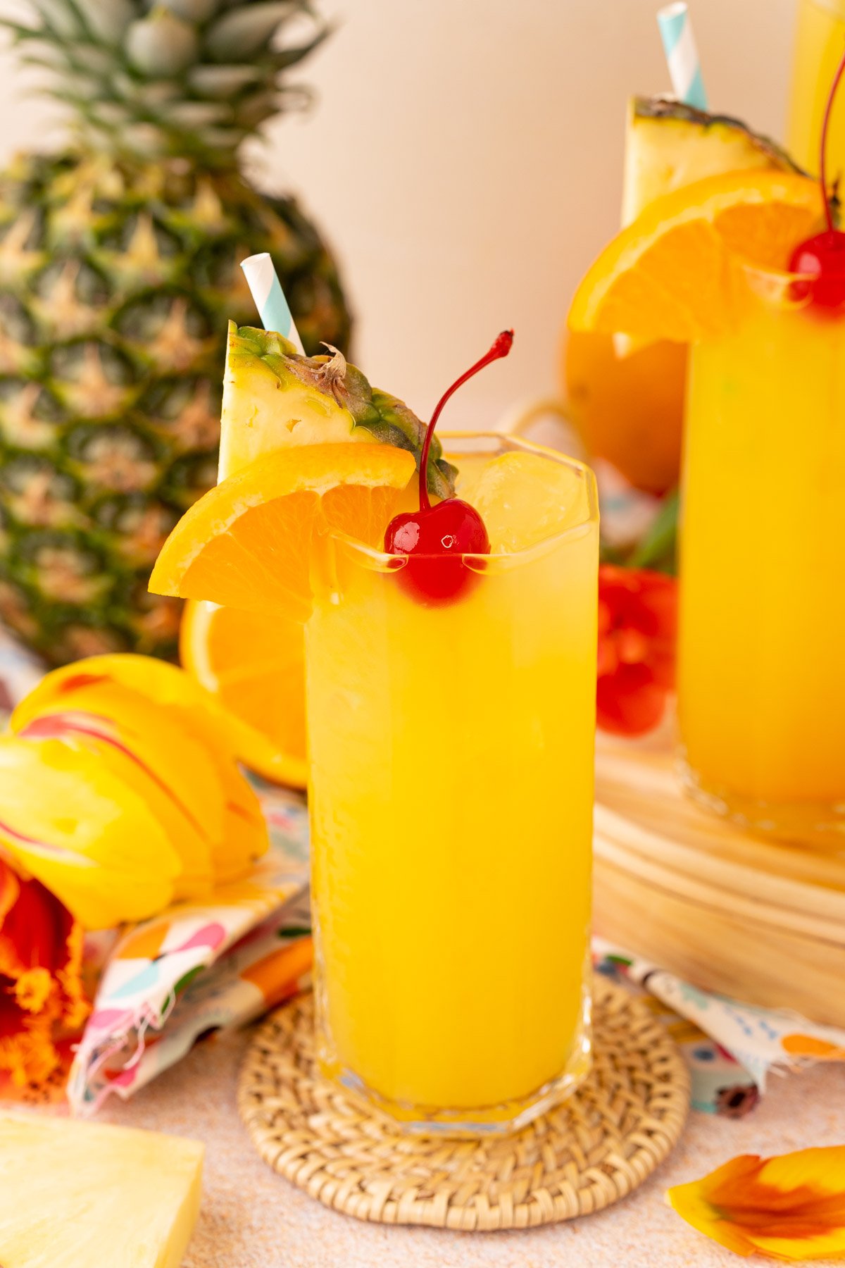 A glass with pineapple punch in it surrounded by flowers and pineapple.