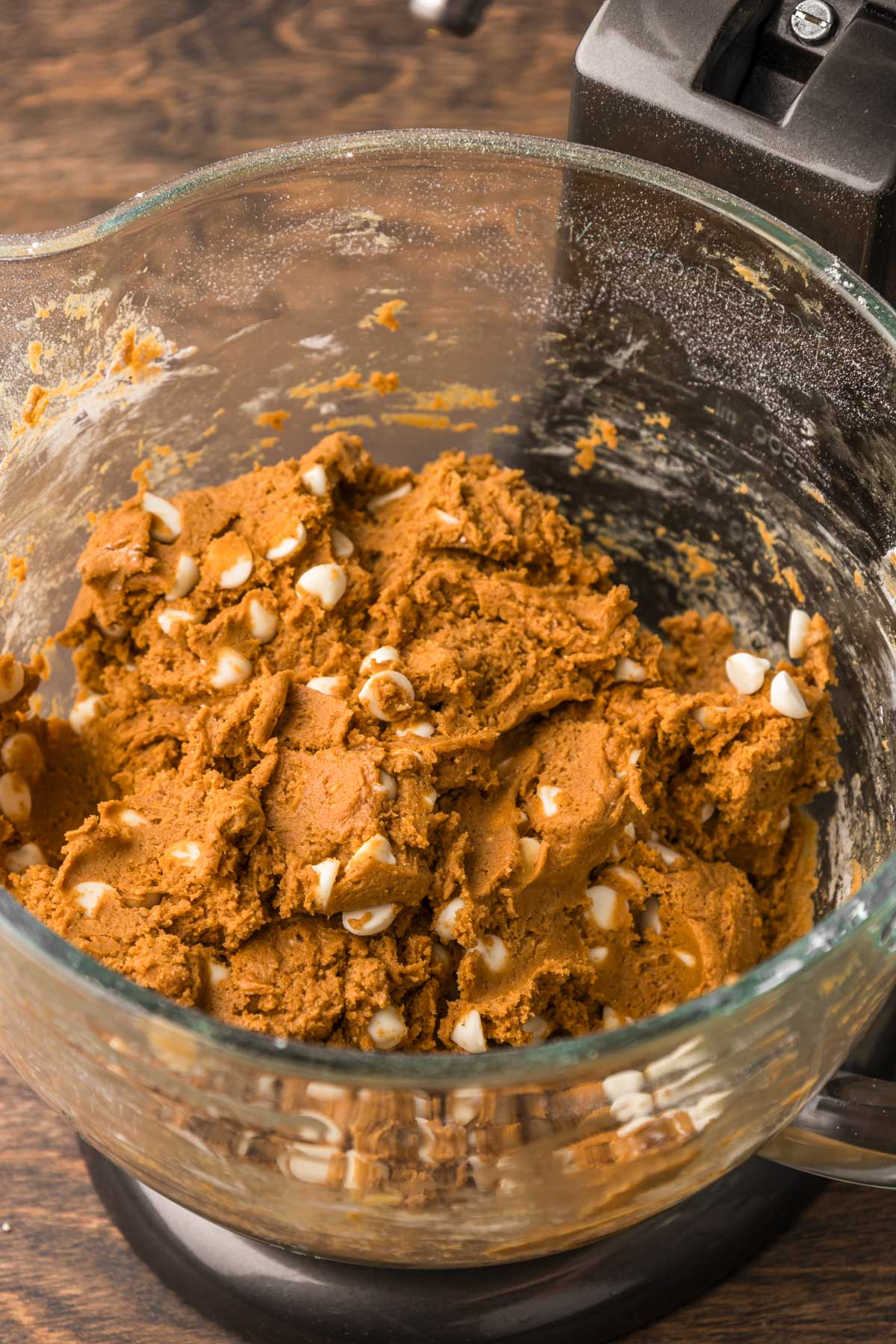 Pumpkin cookies dough with white chocolate chips in a stand mixer bowl.