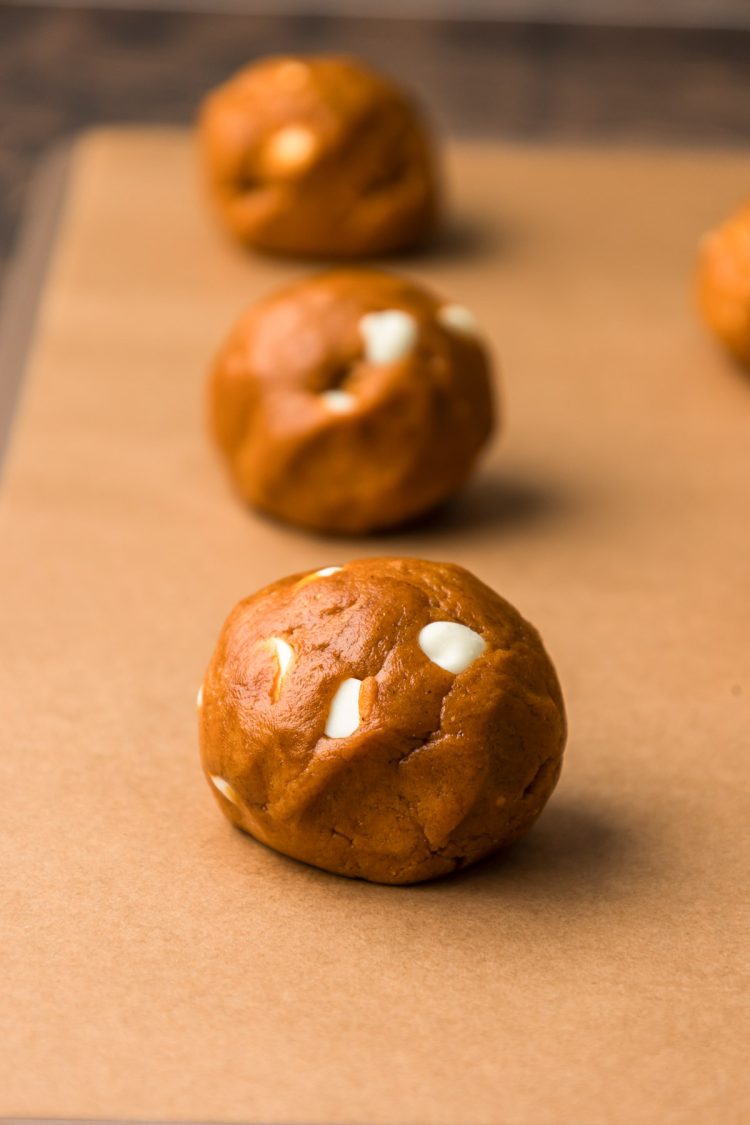 Pumpkin white chocolate chip cookies on a piece of parchment paper on a cookie sheet.