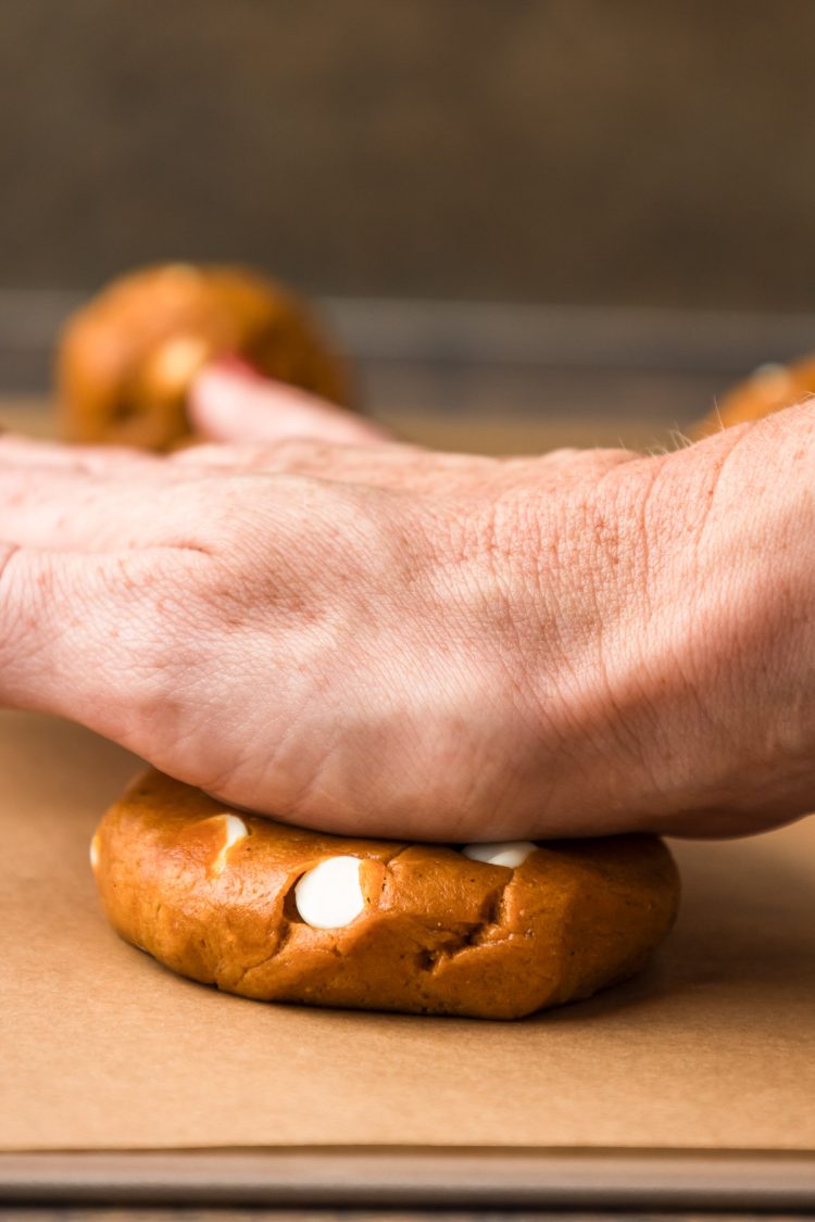 A woman's hand pressing cookie dough down on a baking sheet with her palm.