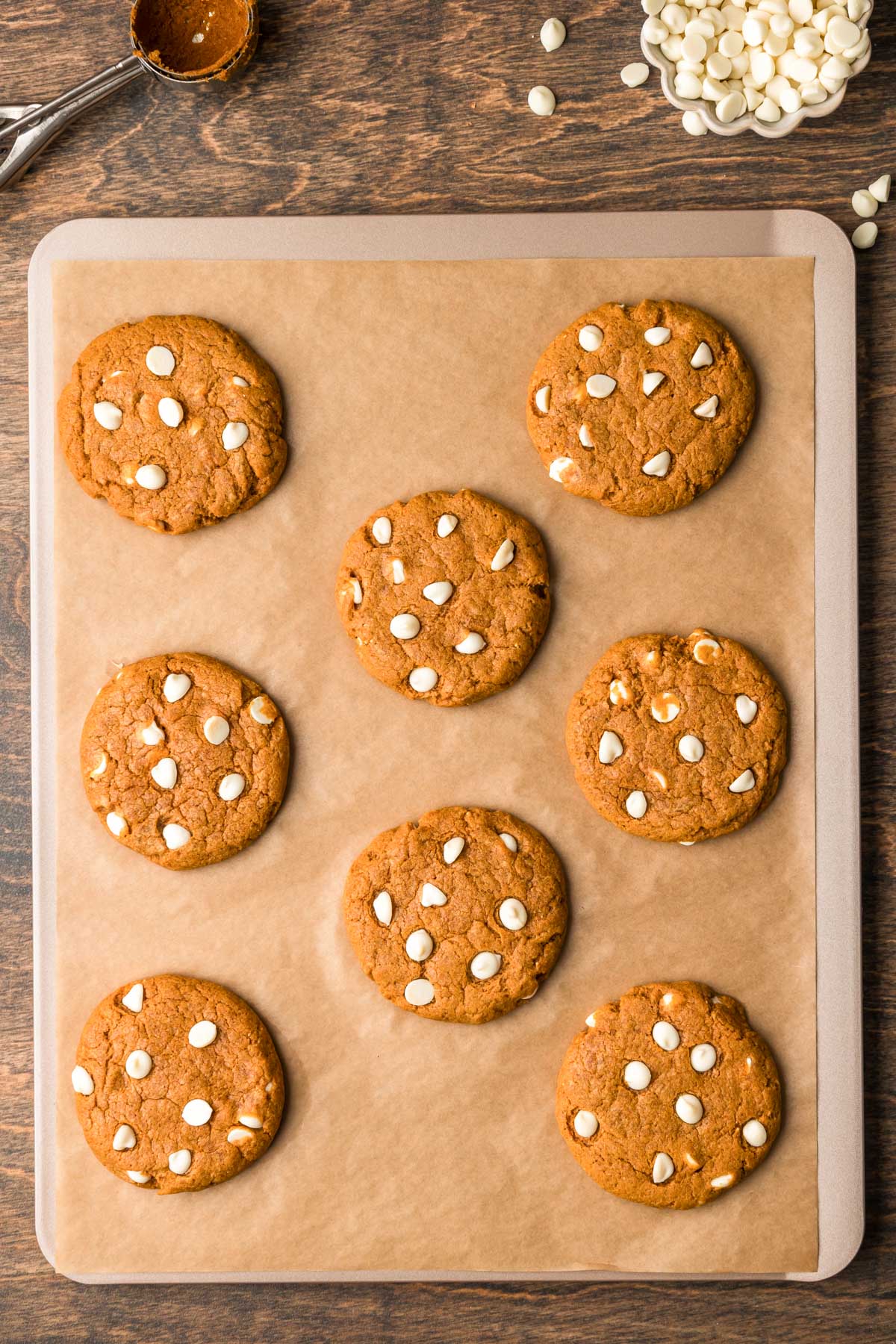 Overhead photo of pumpkin white chocolate chip cookies on a parchment lined baking sheet. 
