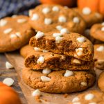 Pumpkin white chocolate cookies on a piece of parchment paper, the top cookies have been broken in half.