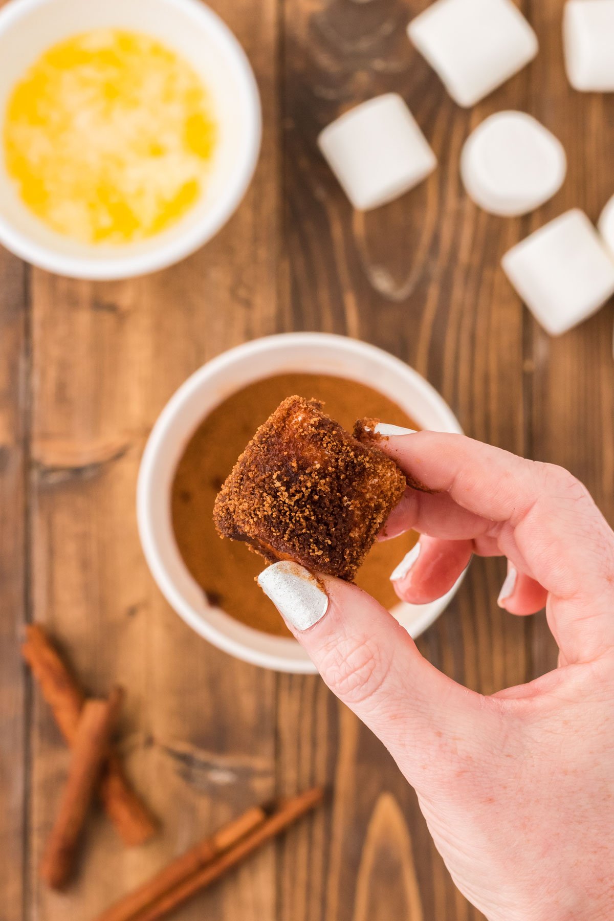 A woman's hand holding a marshmallow that has been coated in brown sugar and cinnamon.