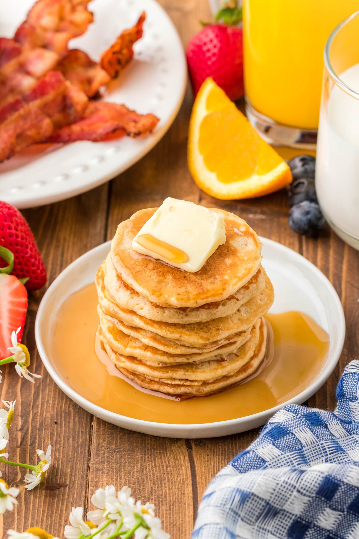 A stack of silver dollar pancakes on a white plate on a wooden table.