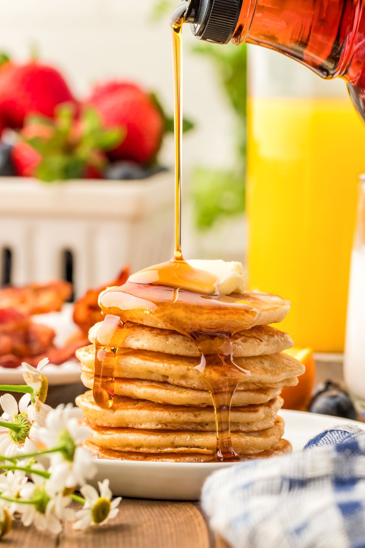 A stack of silver dollar pancakes on a white plate with syrup being poured over the top of them.