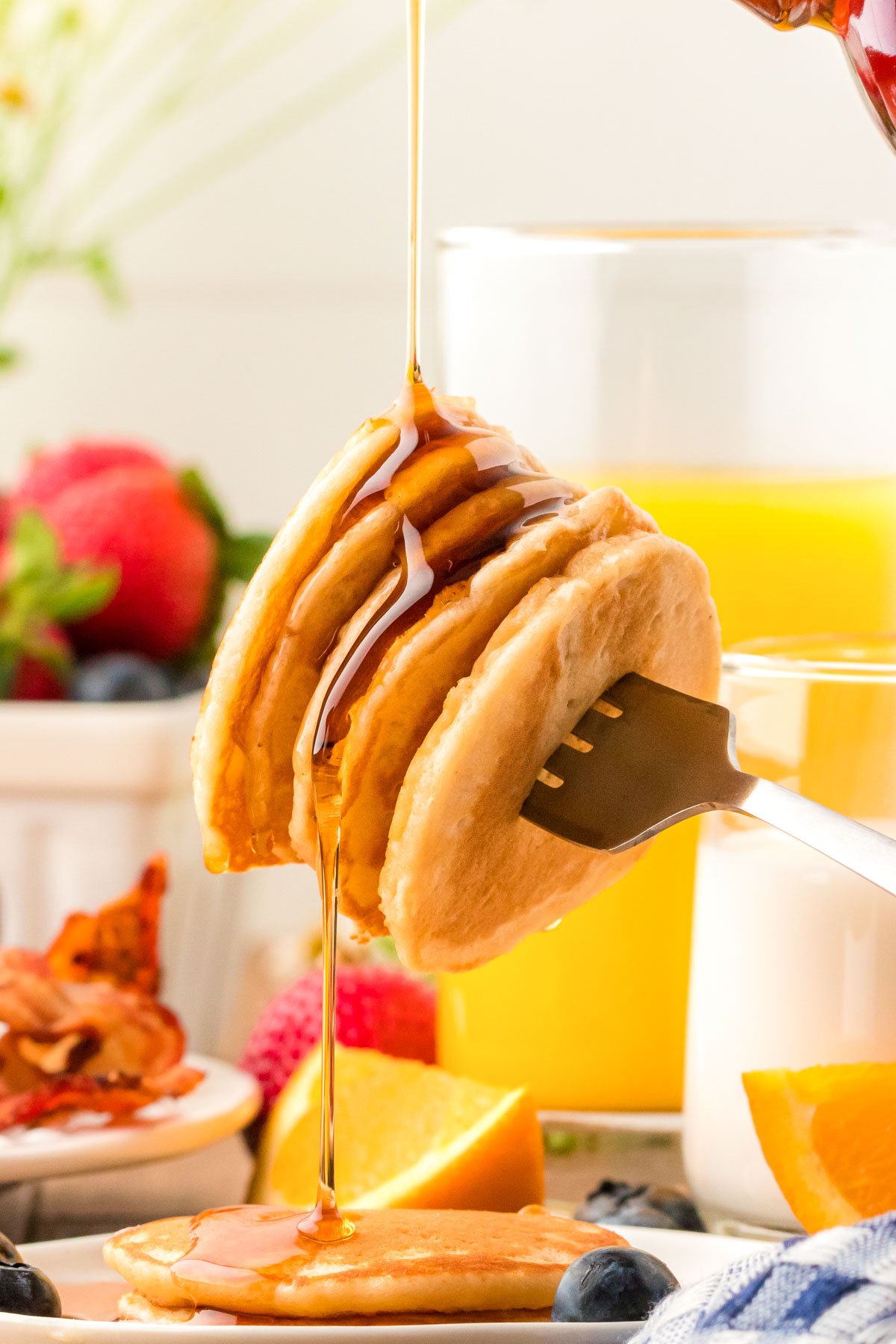 Syrup being poured over a stack of pancakes on a fork.