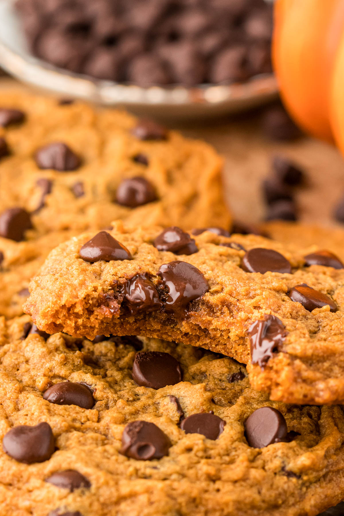 Pumpkin chocolate chip cookies on a table, one is missing a bite.