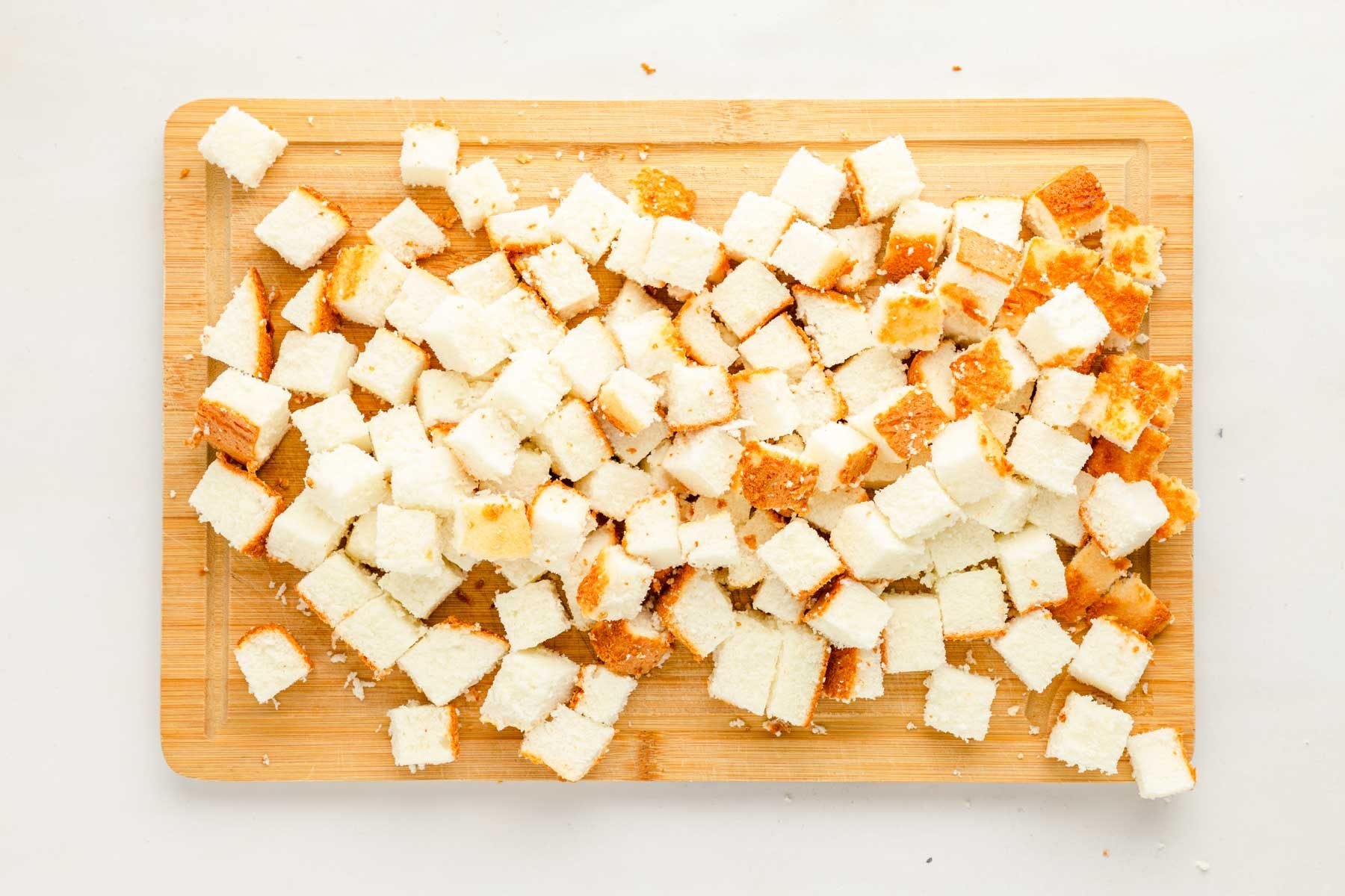 Overhead photo of angel food cake cut into cubes on a cutting board.