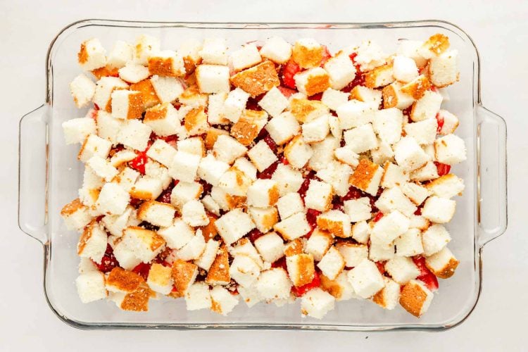 Angel food cake cubes over strawberry filling in a pan.