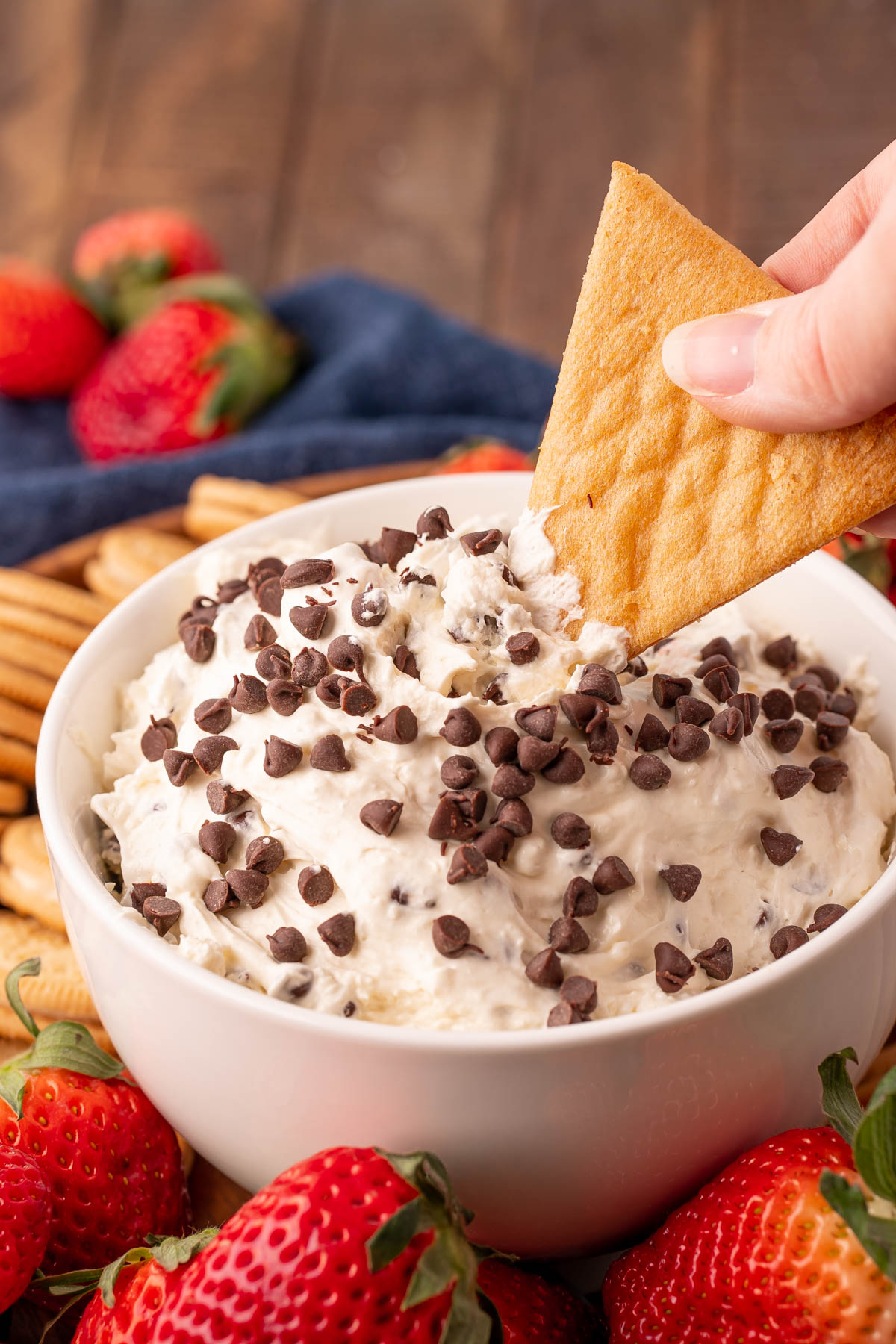 A woman's hand dipping a cookie in a bowl of booty dip.