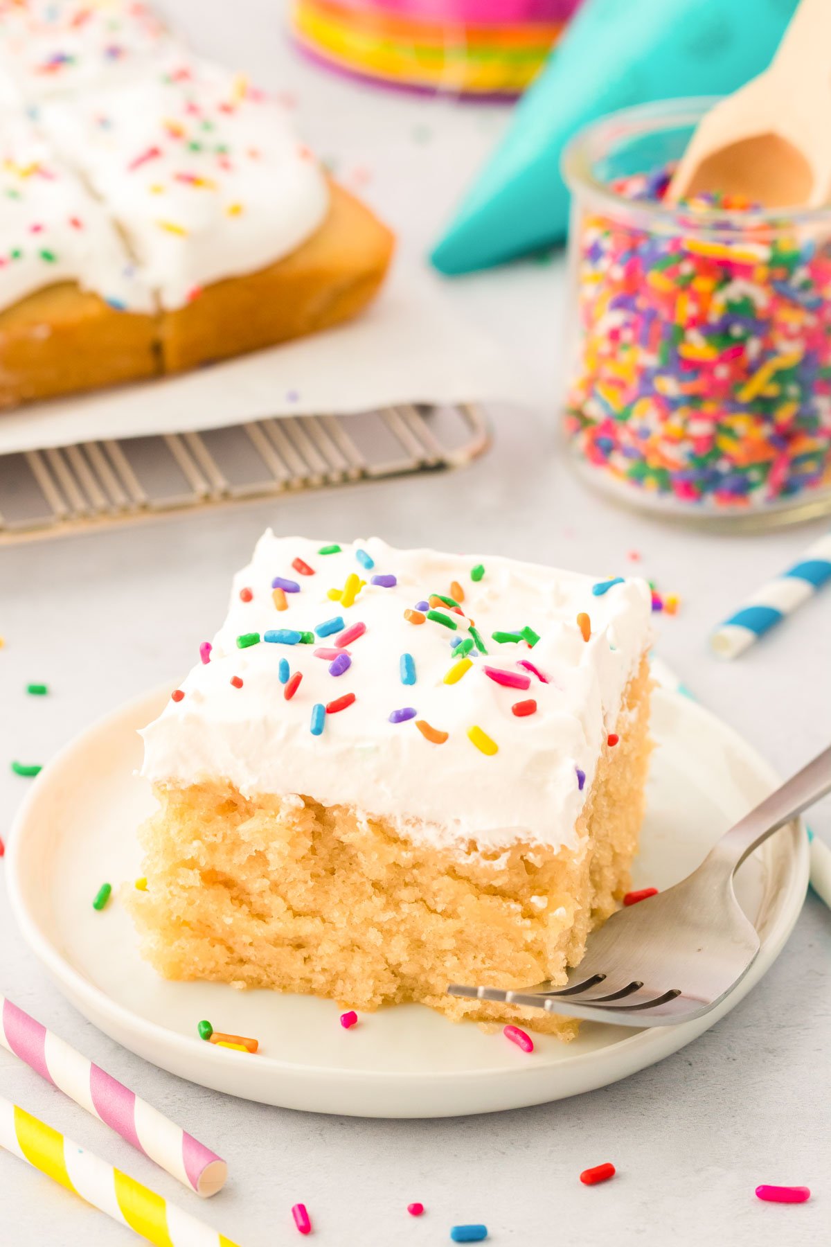 Close up photo of a slice of vanilla crazy cake on a white plate topped with rainbow sprinkles.