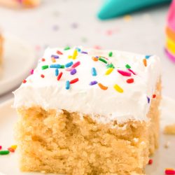 Close up photo of a slice of vanilla crazy cake on a white plate topped with rainbow sprinkles.