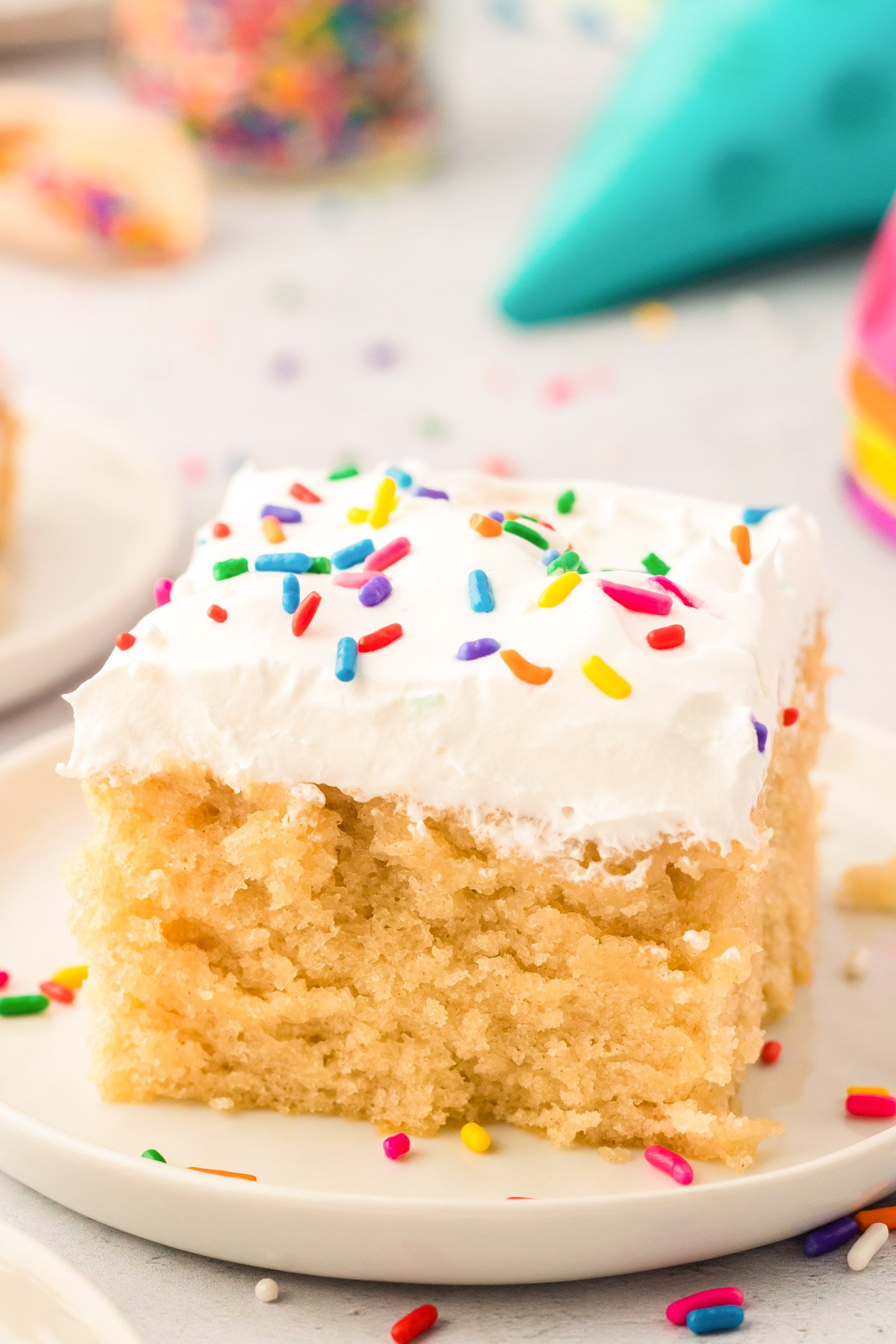 Close up photo of a slice of vanilla crazy cake on a white plate topped with rainbow sprinkles.