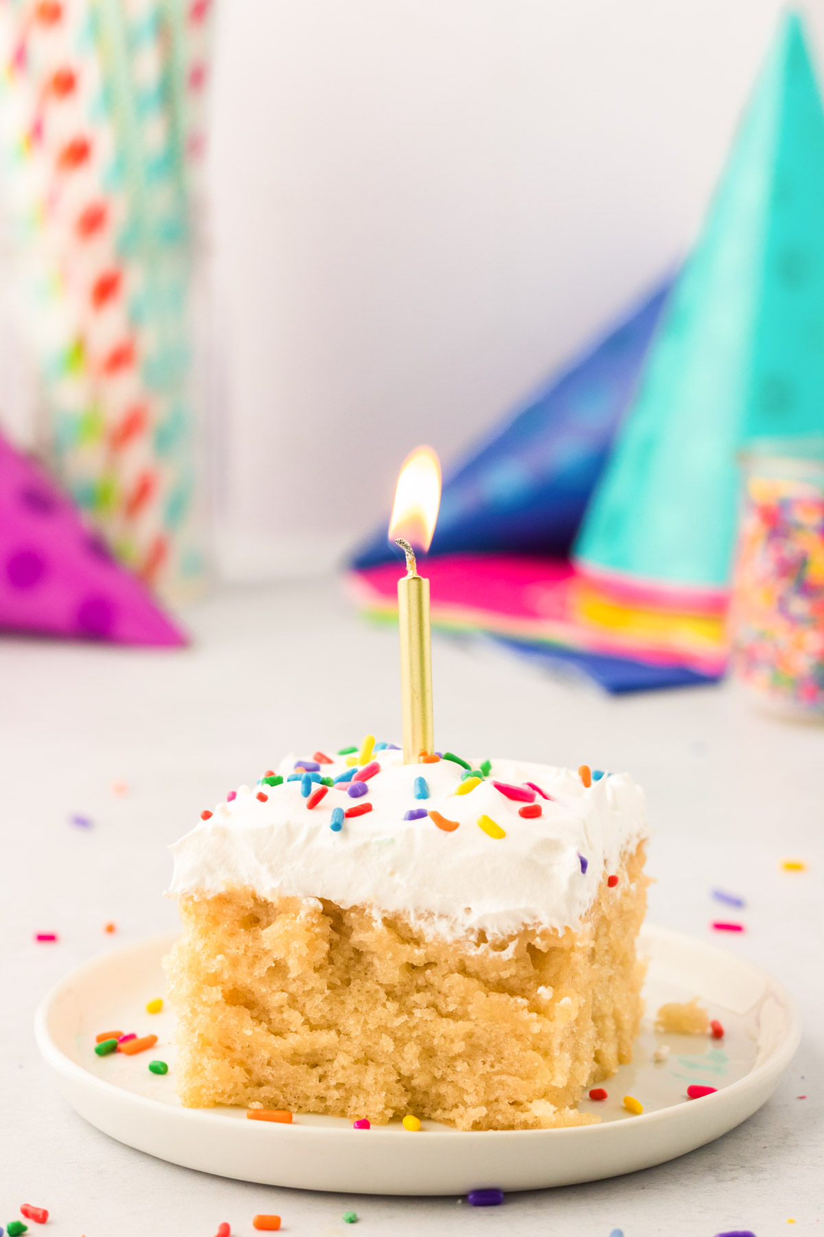 A square slice on vanilla wacky cake on a white plate with a gold birthday candle in it.