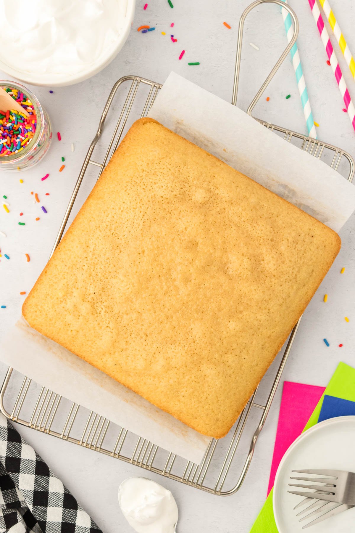 A square vanilla cake cooling on a wire rack.