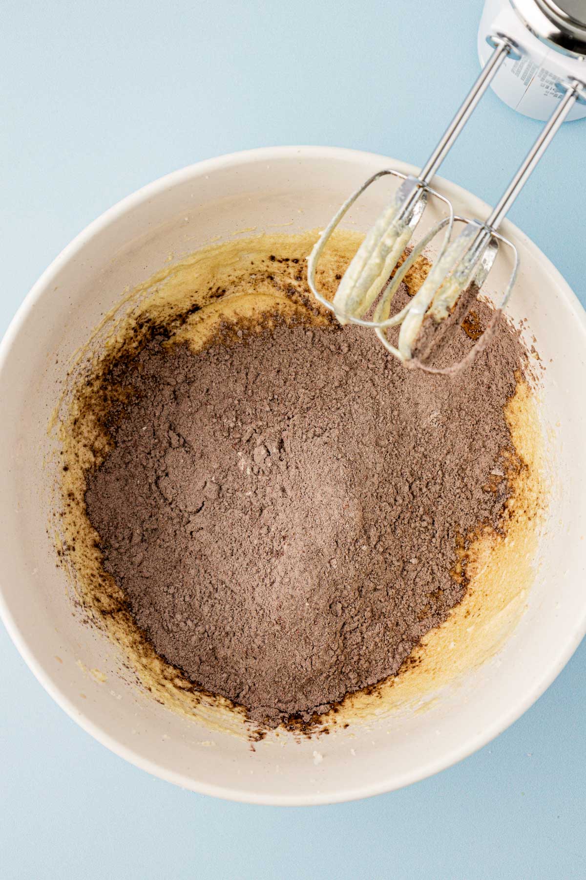 Dry ingredients being added to creamed butter and sugar in a bowl.