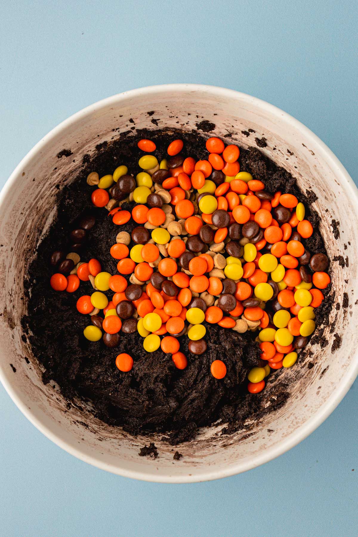 Reese's Pieces and peanut butter chips being added to chocolate cookie dough.