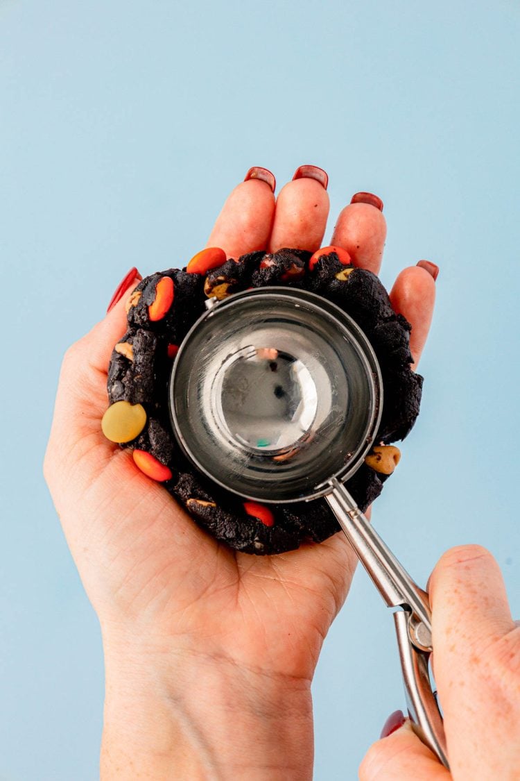 A cookie scoop pressing into a ball of cookie dough in a woman's hand.