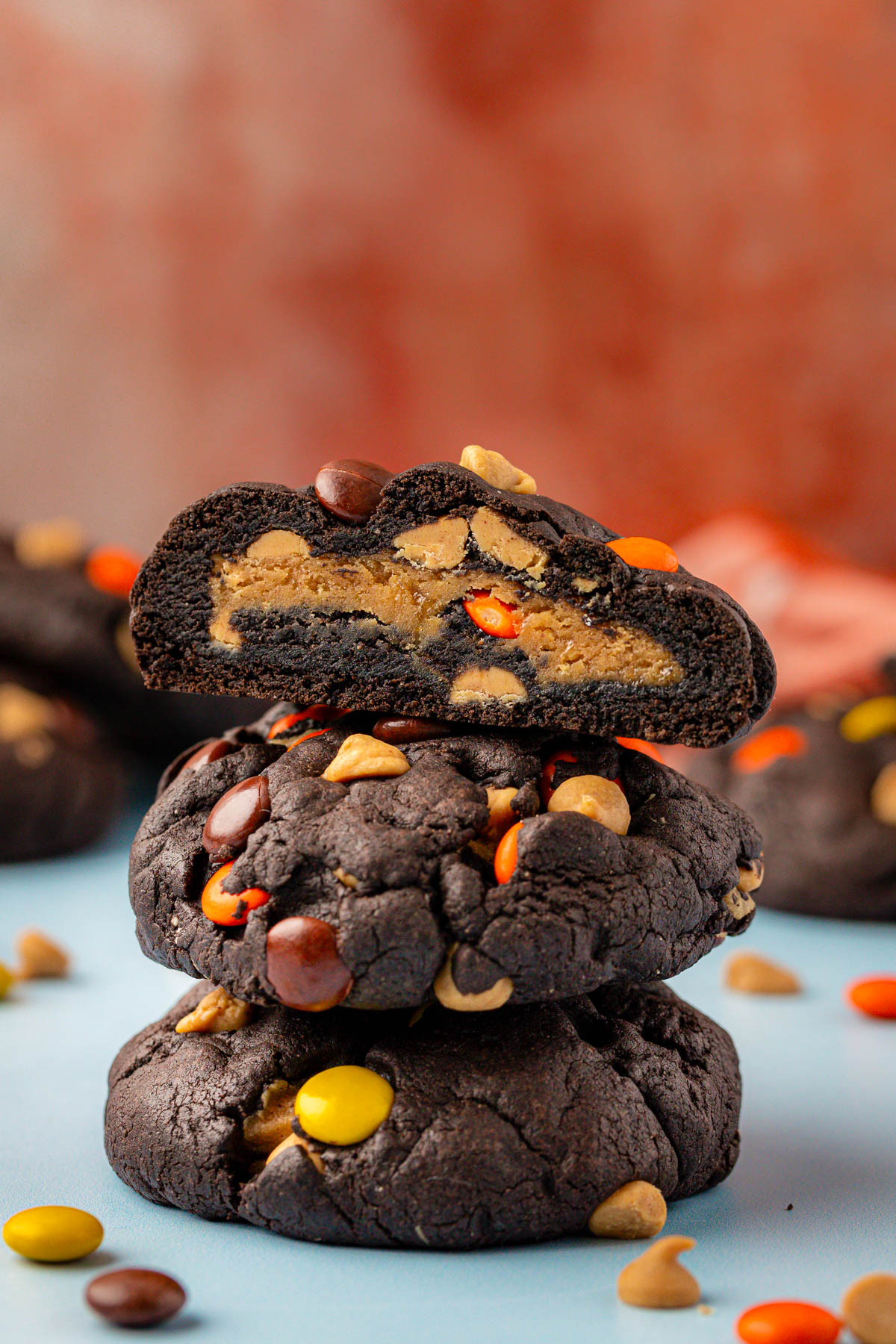 A stack of three chocolate peanut butter cookies, the top one is cut in half to reveal the peanut butter stuffed center.