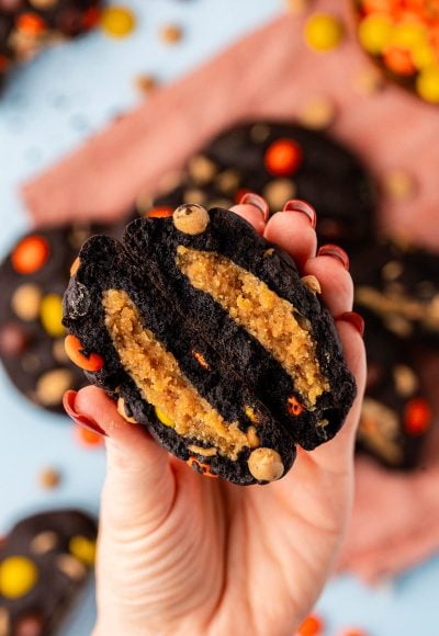 A woman's hand holding a chocolate peanut butter stuffed cookie broken in half to the camera.
