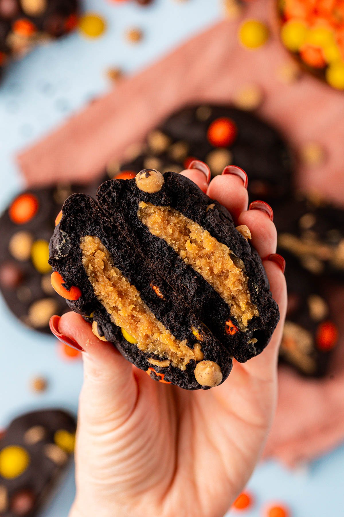 A woman's hand holding a chocolate peanut butter stuffed cookie broken in half to the camera.