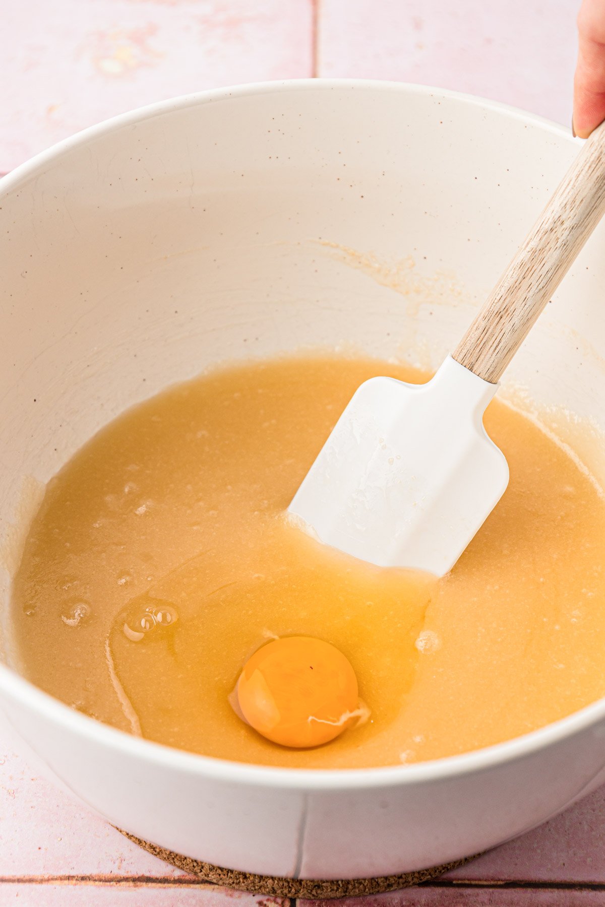 Egg being added to a melted butter and sugar mixture in a bowl.