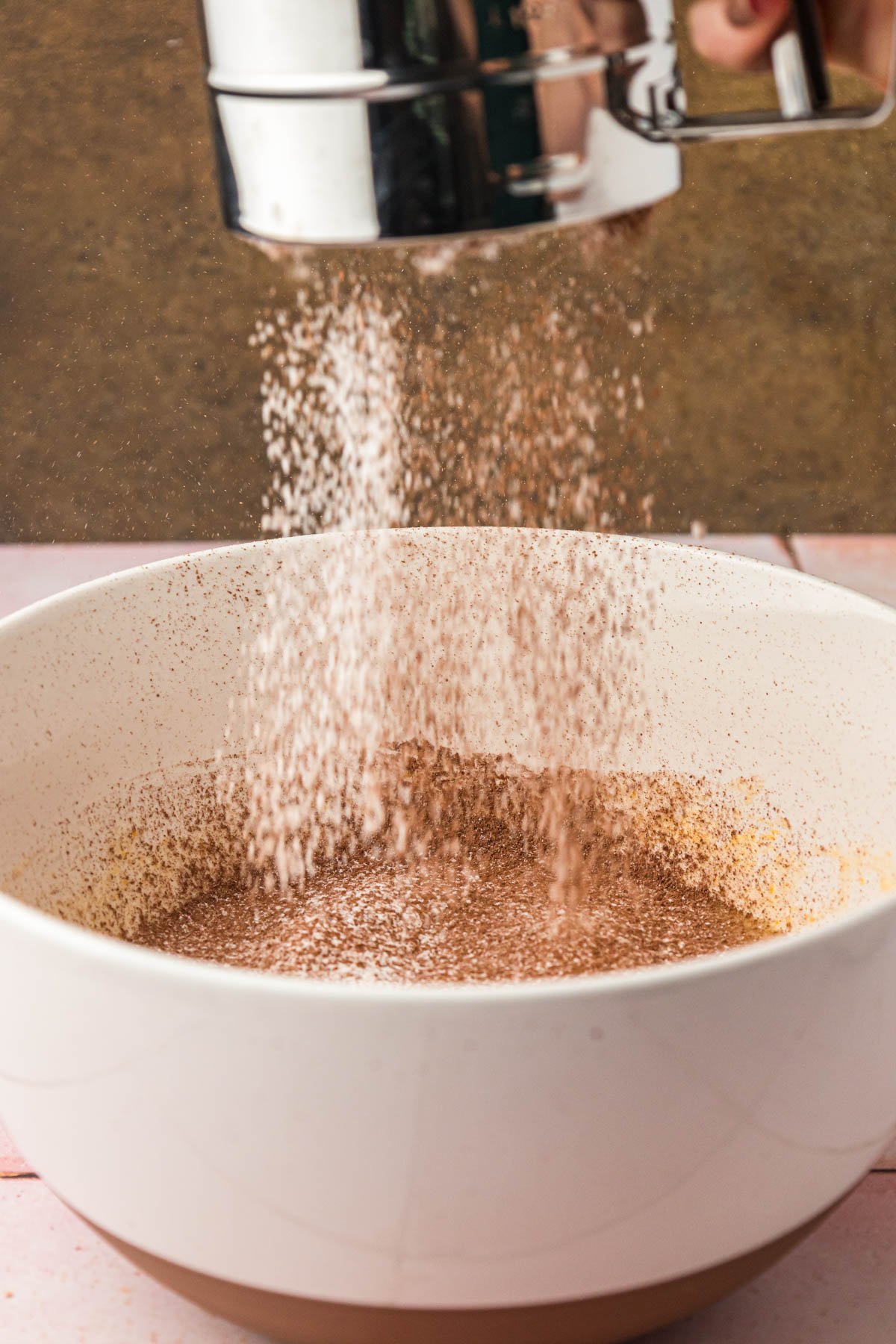 Flour and cocoa powder being sifted into a white bowl to make brownie batter.