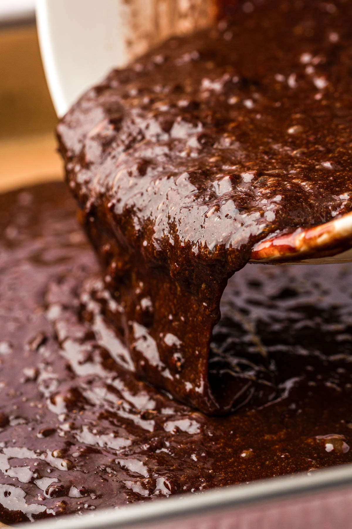 Brownie batter being poured into a parchment lined baking pan.