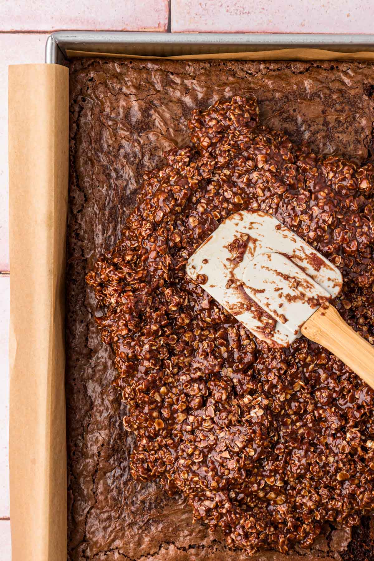 No bake cookie mixture being spread over the top of cooled brownies in a pan.