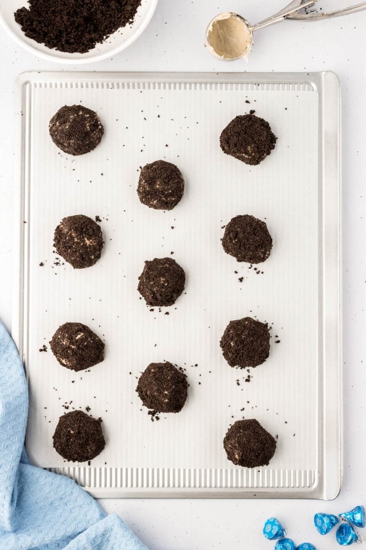 Cheesecake cookies coated in Oreo crumbs on a parchment lined baking sheet.