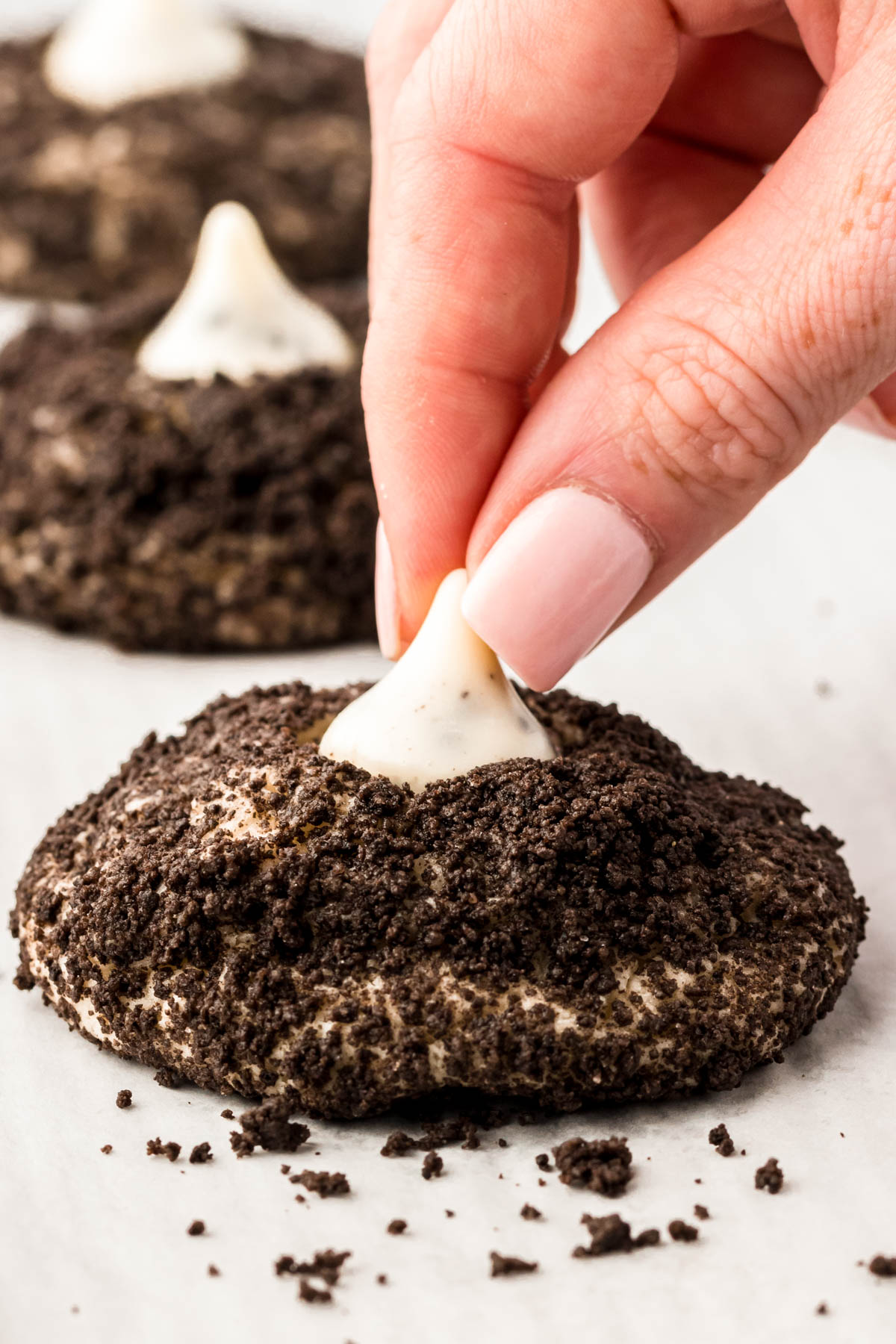 A cookies and cream Hershey Kiss being pressed into an Oreo crumb covered cookies.